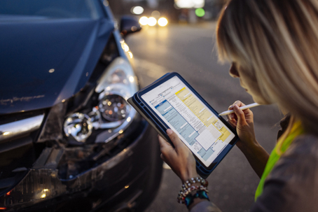Person documenting car damage on a tablet after an accident, representing communication with insurance companies in Oregon.